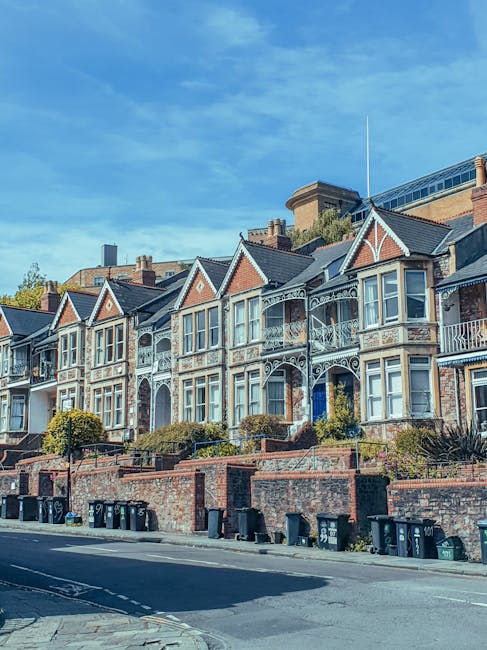 A row of Victorian-style terraced houses with ornate white ironwork balconies and large sash windows, situated on a sloped street in Wandsworth. The houses are constructed with brick and have decorati